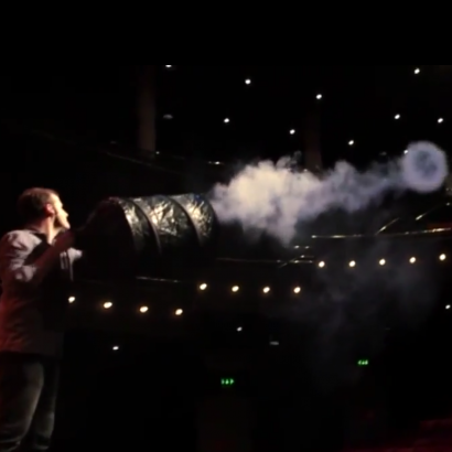 A performer blowing smoke rings from a device on stage